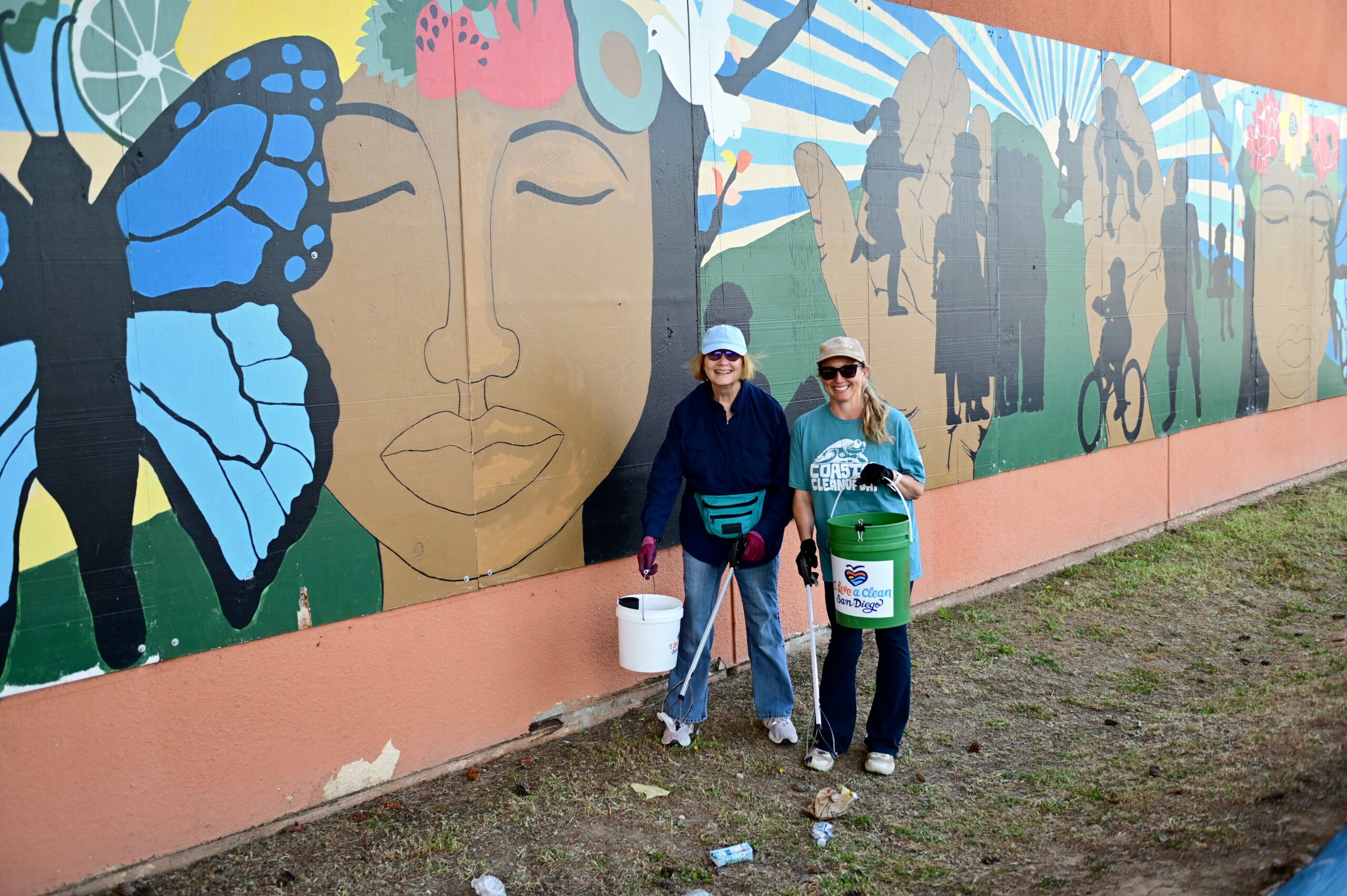 Two volunteers at I Love A Clean San Diego's Creek to Bay cleanup pick up trash in front of a mural.