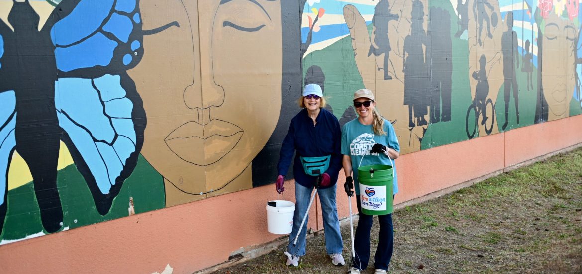 Two volunteers at I Love A Clean San Diego's Creek to Bay cleanup pick up trash in front of a mural.